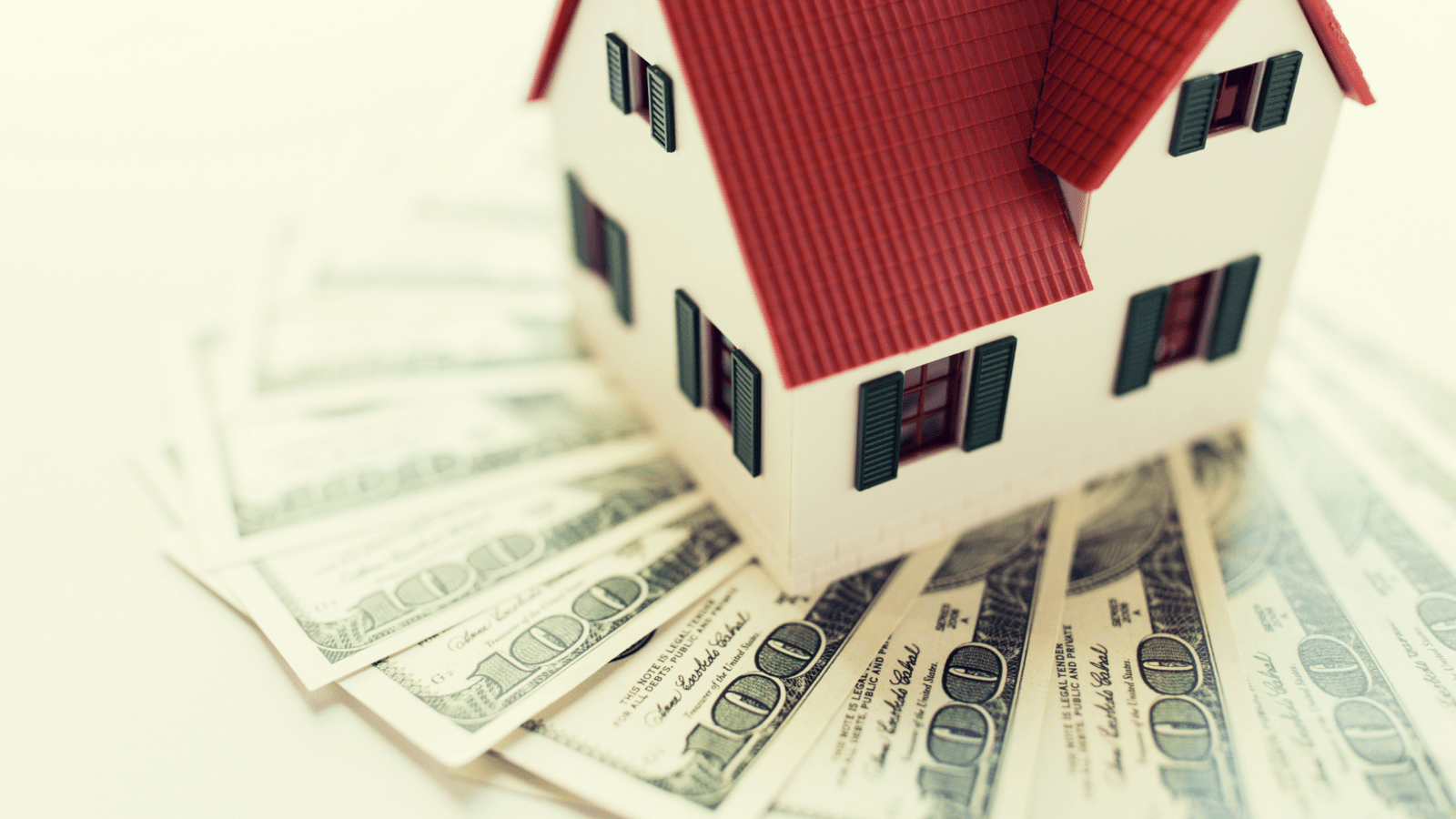a toy house sitting on top of spread out hundred dollar bills